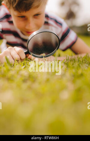 Kid giocando con lente di ingrandimento all'esterno. Ragazzo di esplorare il giardino con lente di ingrandimento in corrispondenza del parco. Foto Stock