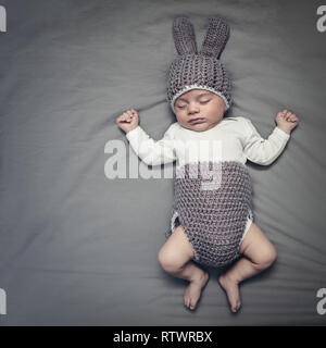 Carino piccola Pasqua baby bunny, piccola e dolce bambino che dorme vestito in funny coniglio costume sistemata sulla coperta grigio Sfondo, vacanze di Pasqua foto wit Foto Stock