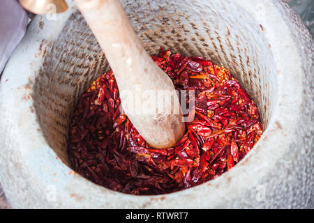 La macinazione secchi peperoncino rosso in un contenitore di pietra. Foto Stock