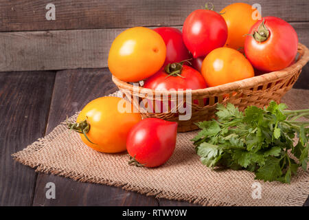 Il giallo e il rosso dei pomodori in un cesto di vimini sul tavolo di legno Foto Stock