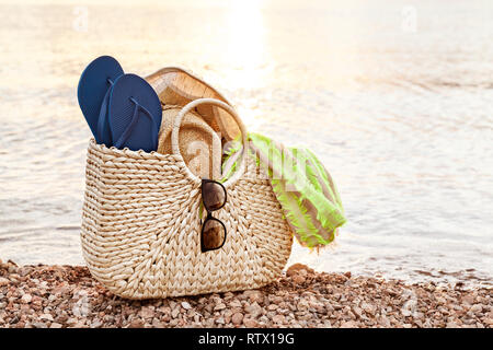 Borsa di paglia, cappello, occhiali da sole e Flip Flop sulla spiaggia al tramonto in estate Foto Stock