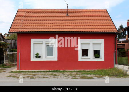 Completamente rinnovato suburbana di piccola casa di famiglia con il nuovo Windows e tegole circondato da erba non tagliata e ghiaia accanto alla strada asfaltata Foto Stock