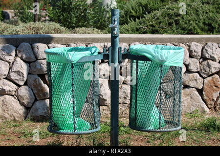 Verde palo metallico con doppio pubblico outdoor trash lattine con nuove borse in nylon inserita e posacenere rotto sulla parte superiore con il tradizionale muro di pietra Foto Stock