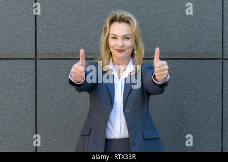 Entusiastico motivati attraente giovane donna dando un pollice in alto gesto di approvazione e di successo con un sorriso raggiante Foto Stock