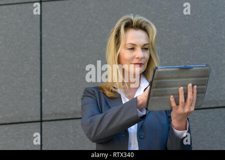 Coppia imprenditrice utilizza un dispositivo tablet per navigare in internet come ella pause nella parte anteriore del grigio di un muro di pietra in città Foto Stock