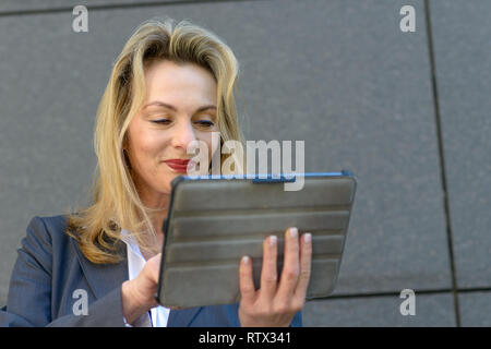 Coppia imprenditrice utilizza un dispositivo tablet per navigare in internet come ella pause nella parte anteriore del grigio di un muro di pietra in città Foto Stock