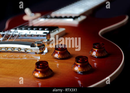 Close up del controllo di volume e di tono di colore rosso ciliegia con la chitarra elettrica con ponte e stringhe in background Foto Stock