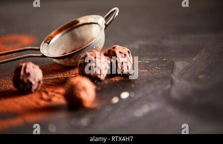 Bonbons di cioccolato spolverati con polvere di cacao su un bancone cucina a fianco di un vaglio metallico e spazio di copia Foto Stock