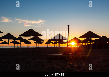 Tramonto in holiday resort sulla costa turca con ombrelloni sulla spiaggia. Calma il cielo blu e arancione Sun su orizzonte bassa Foto Stock