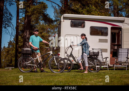 Donna con un uomo sulla bicicletta elettrica in appoggio al campeggio. Vacanza per la famiglia in viaggio, viaggio vacanza in camper RV, Caravan auto vacanza. Foto Stock