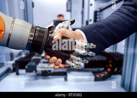 La mano di un uomo d'affari che stringono le mani con un robot androide. Il concetto di interazione umana con intelligenza artificiale. Foto Stock