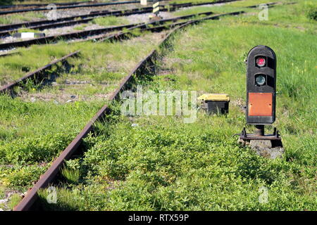 Luce rossa sulla ferrovia il traffico a terra luce segnale montate su piastra in acciaio e calcestruzzo accanto ai binari ferroviari circondato da erba non tagliata Foto Stock