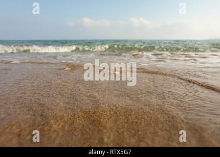 Sabbia bagnata sulla spiaggia, mare in distanza, angolazione bassa foto a livello del suolo, lente coperto con alcune gocce di sottolineare l'acqua. Abstract sfondo marino. Foto Stock