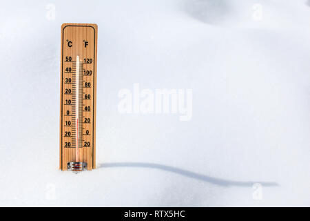 Termometro in legno in piedi nella neve, che mostrano una bassa temperatura, spazio per il testo a destra. L'inverno prossimo concetto. Foto Stock