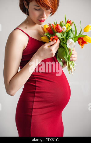 Donna incinta in abito rosso con un bouquet di tulipani Foto Stock