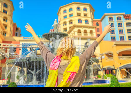 Carefree donna bionda gode di fontane ad acqua nel centro di Medina, una esclusiva zona residenziale di La Perla Qatar, icona di Doha, Golfo Persico, medio Foto Stock