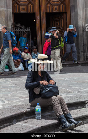 Quito, Ecuador, Agosto 2018: una donna non identificato controlla il suo portafoglio mentre prendendo una pausa seduta sui gradini della chiesa di San Francisco Foto Stock