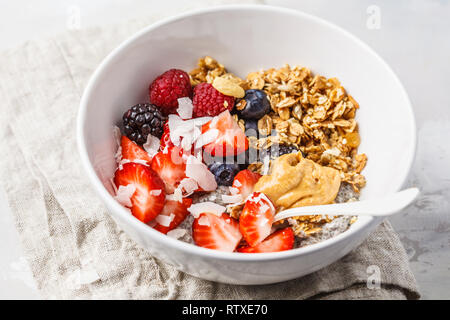 Bacche, granola, latte, burro di arachidi Prima colazione in una ciotola bianco. Sano cibo vegan concetto. Foto Stock