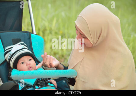 Musulmani asiatici hijabi il padre e la madre a piedi attraverso il parco con il figlio in passeggino mentre la sua mamma di prendersi cura di lei todler Foto Stock