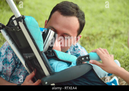 Padre a piedi attraverso il parco con il figlio in passeggino mentre baciare il suo figlio Foto Stock