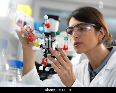 Donna scienziato progettare una formula chimica utilizzando una pallina e stick modello molecolare in laboratorio. Foto Stock