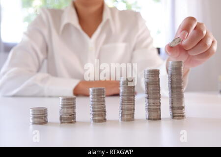 Persona d'affari immissione moneta oltre il crescente monete Stack. Foto Stock