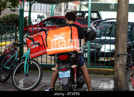 Lima, Perù - 17 Febbraio 2019: guidatore giovane ragazzo che lavora per Rappi una consegna del cibo, servizio parcheggiato al di fuori di un parcheggio. Condivisione di economia collaborativa Foto Stock