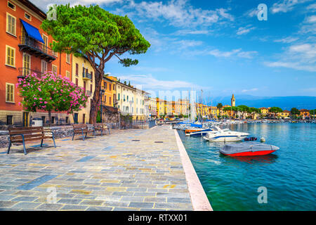 Splendido viale lastricato con colorati fiori mediterranei. Yacht di lusso, barche e barche a vela nel maestoso porto di Toscolano-Maderno, lago Foto Stock