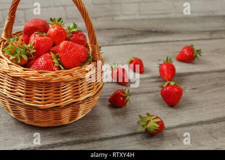 Cesto di Fragole, alcuni di loro versato sul legno grigio desk. Foto Stock