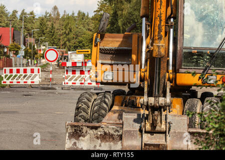 Dettagli su vecchie gialle macchina di scavo torna, cabina del conducente visibile, strada chiusa segni, terreno scavato e rimosso asfalto, in background. Roadworks concept Foto Stock