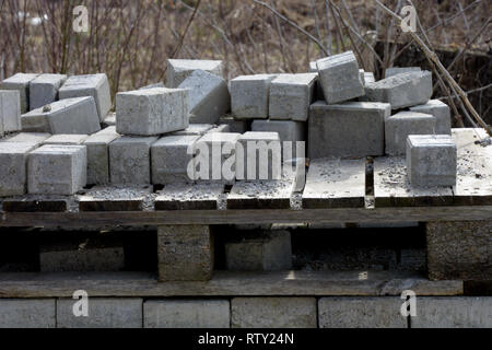 Pila di cemento grigio dei blocchi utilizzati per pavimentazioni, marciapiedi, impilate di blocchi in calcestruzzo su un marcio pallet di legno nella costruzione area del sito Foto Stock