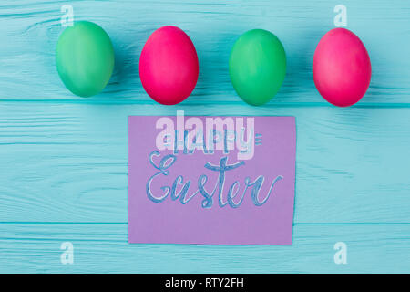 Fila di Pasqua uova colorate e carta. Quattro verde e rosso uova di Pasqua e biglietto di auguri. Le idee di saluto pasquale per i bambini. Foto Stock