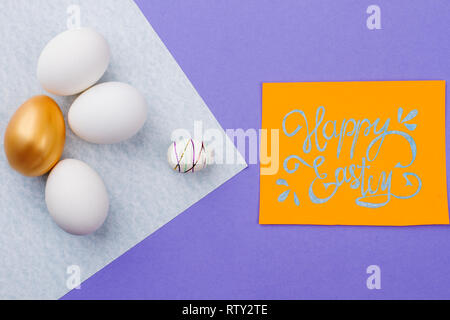 Felice Pasqua manoscritta carta di credito. Tre le uova bianche e una golden egg sul foglio di carta. Felice Pasqua composizione. Foto Stock