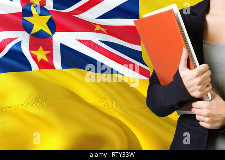 Apprendimento del linguaggio concetto. Giovane donna in piedi con la bandiera di Niue in background. Docente in possesso di libri, arancione sbozzato per la copertina del libro. Foto Stock