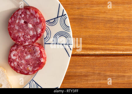 Alcune fette di salame su una vecchia piastra ceramica su una tavola di legno tavolo rustico. Cibo per uno snack Foto Stock