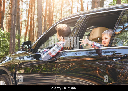 Bambino caucasico ragazzo in camicia a scacchi guardando fuori dalla finestra mentre suo padre alla guida di un'auto. Viaggio sicuro, viaggio di concetto guida. Foto Stock