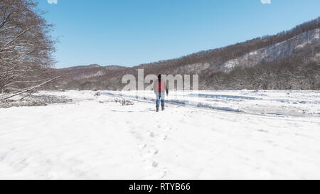 Un uomo solitario passeggiate lungo la congelati letto di un fiume di montagna Foto Stock