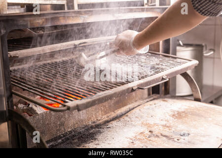 Cibo, artigianato e salsicce concetto - uomo salsicce di cottura su una griglia piana Foto Stock