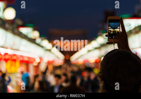 Visite turistiche e la fotografia in Tokyo. Scattare foto con il cellulare lungo la famosa Nakamise Shopping Street in Asakusa durante la notte Foto Stock