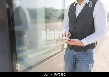 Giovani e casual uomo d affari utilizzando Tablet mentre si cammina al di fuori dell'edificio degli uffici Foto Stock