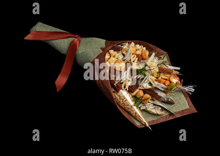 Decorate in modo originale regalo per una festa della birra in forma di un bouquet di essiccato pesce salato, arachidi, cracker e altri snack su sfondo nero Foto Stock
