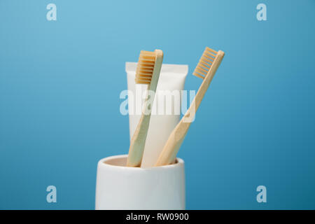 Titolare con il dentifricio nel tubo di bambù e di spazzolini da denti su sfondo blu Foto Stock