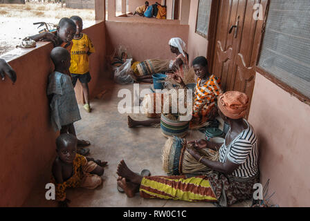 Una foto di donne ghanesi, seduto su un balcone e rendendo il famoso Bolgatanga cestini di mercato mentre i loro bambini stanno guardando e l apprendimento Foto Stock