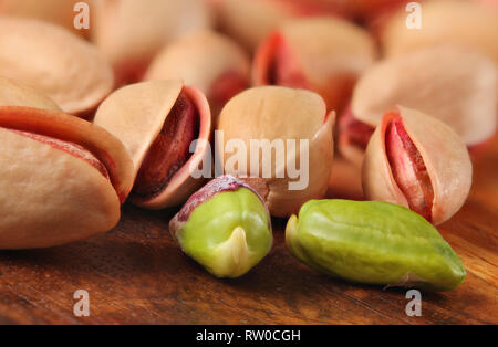 Primo piano della Rossa turca pistacchi tostati e salati, due di essi, pelati, dado verde visibile, sulla tavola di legno. Foto Stock