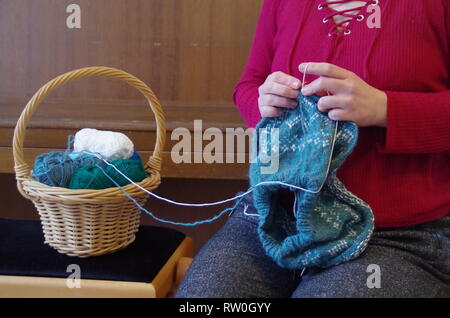 Una donna di lavorazione a maglia di un pullover con norewgian pattern e un cestello con palline di lana Foto Stock