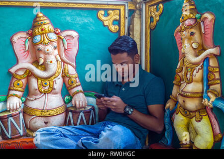 Corte Hill Ganesh tempio indù, Kuala Lumpur, Malesia. Giovane uomo con un telefono cellulare accanto a Ganesh scultura. Foto Stock