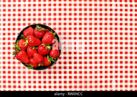 Vista del piano portapaziente, nero piccolo vaso in ceramica di fragole sul rosso Gingham a scacchi la tovaglia Foto Stock