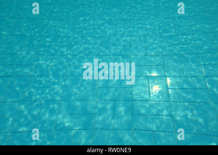Piscina fondo, il sole che splende su piastrelle blu, linee distorta dalla rifrazione in acqua. Foto Stock