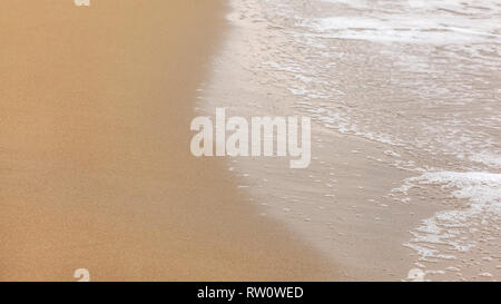 Sabbia bagnata sulla spiaggia, resti di acqua con schiuma bianca che mostra sulla destra, nuvoloso giorno. Abstract sfondo del mare. Foto Stock