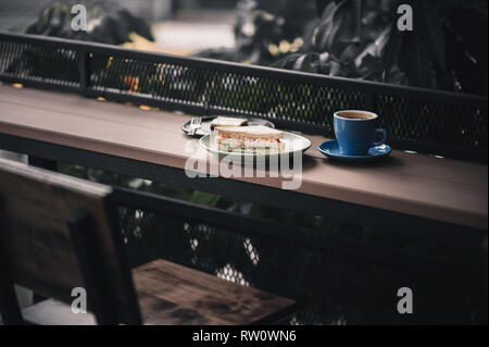 Abstract Scena di prima colazione pasto impostare compresi tonno sandwich, hot lungo nero caffè e brownie cheese cake su legno outdoor bar. Fine settimana mattina acti Foto Stock